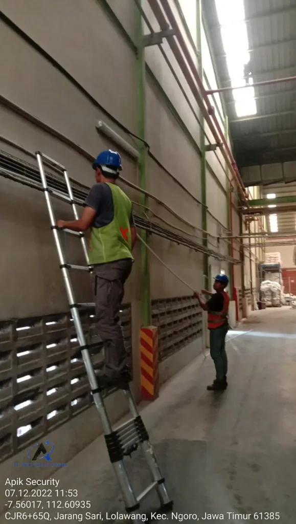 Tim teknisi CCTVSurabaya.com sedang melakukan pemasangan jalur pipa conduit dan kabel CCTV di dinding area gudang pabrik kawasan Ngoro Industrial Park, Mojokerto.