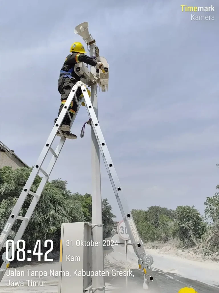 Teknisi CCTVSurabaya.com dengan standar safety lengkap melakukan perawatan sistem CCTV yang terintegrasi dengan Horn Speaker (Public Address) di tiang tinggi kawasan industri Gresik.