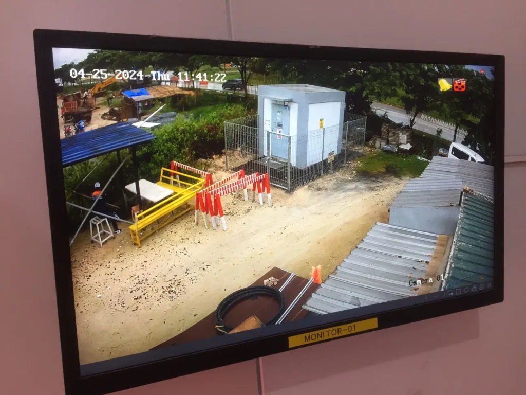 Tampilan layar monitor CCTV resolusi tinggi menampilkan aktivitas area proyek konstruksi dan pos keamanan di Surabaya, hasil instalasi CCTVSurabaya.com.